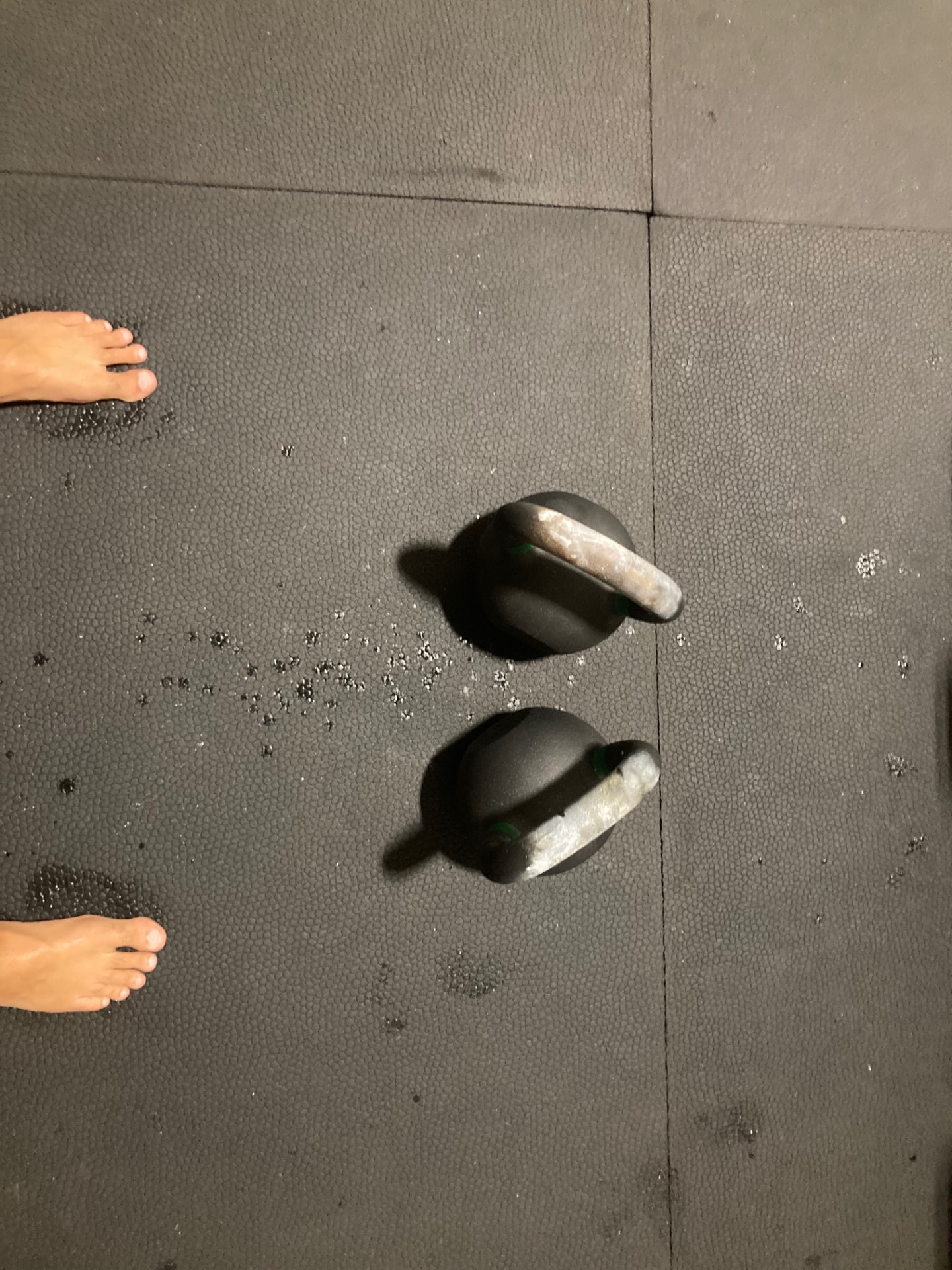 Two chalked kettlebells set on the floor before a double bell set