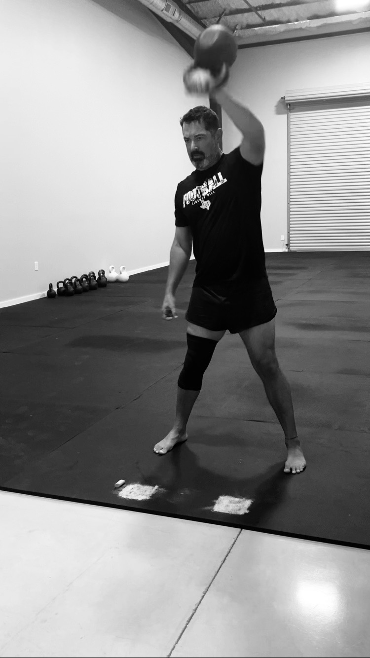 Coach finishing a one-arm kettlebell snatch overhead at Liberty Bells