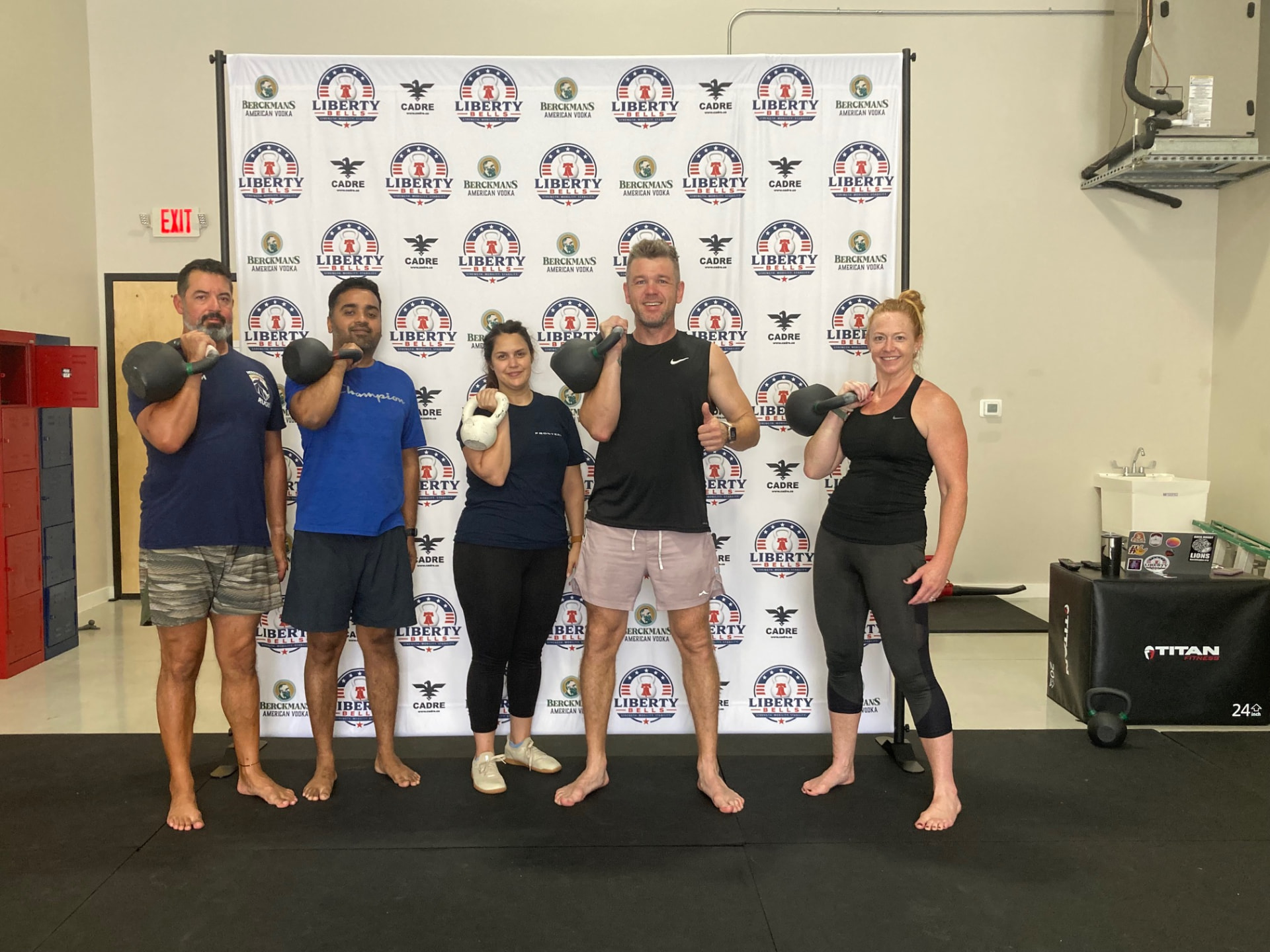 Liberty Bells members holding kettlebells in the rack position in front of the sponsor backdrop
