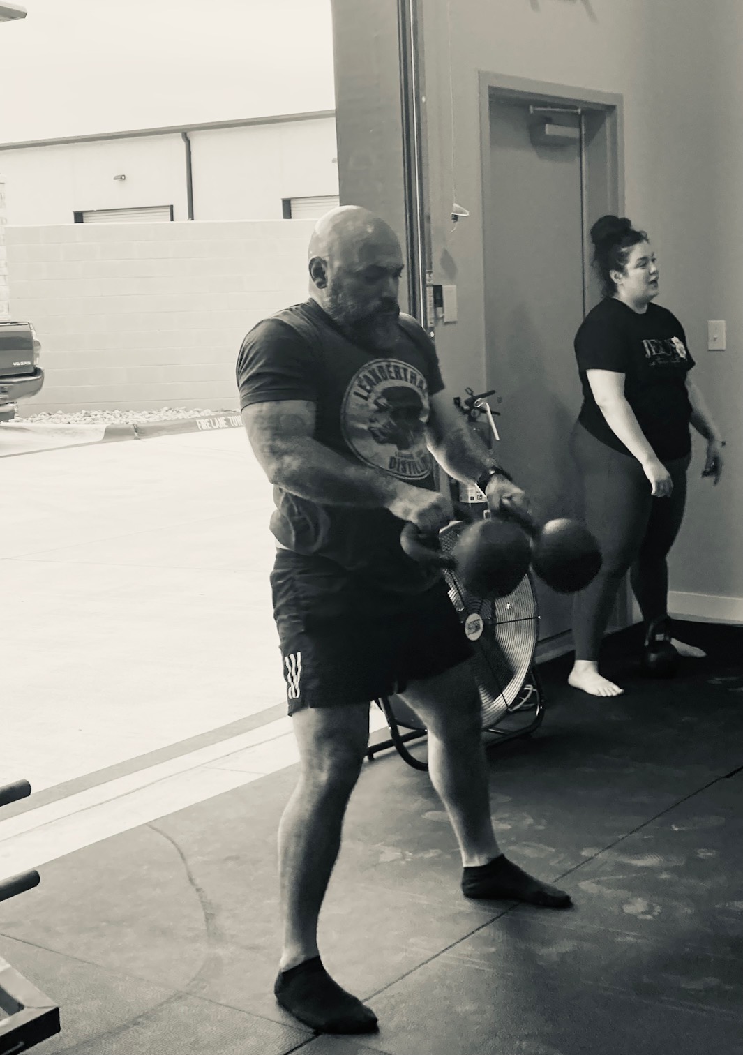 Member performing double kettlebell swings by the roll-up door at Liberty Bells