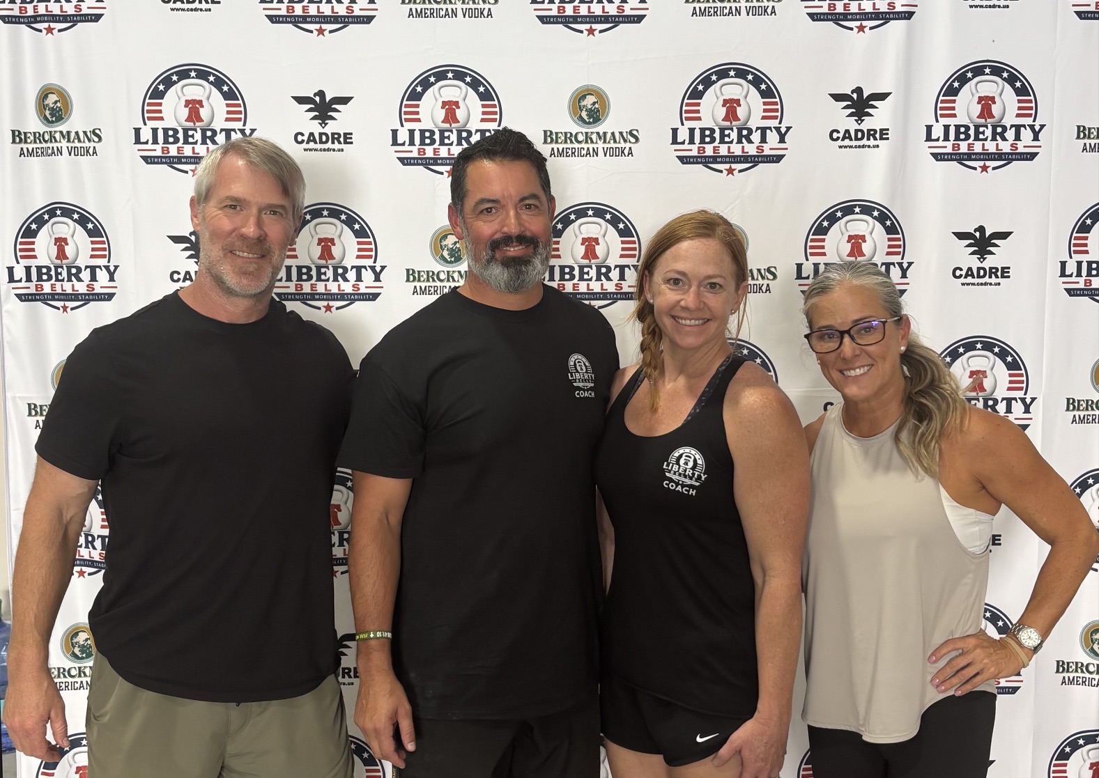 Liberty Bells coaches and guest coaches smiling in front of the sponsor backdrop